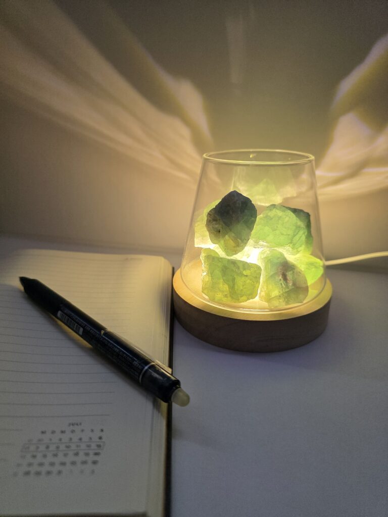 Still. jade stone lamp glowing softly on wooden base beside an open journal and pen — natural green jade ambient light for slow living